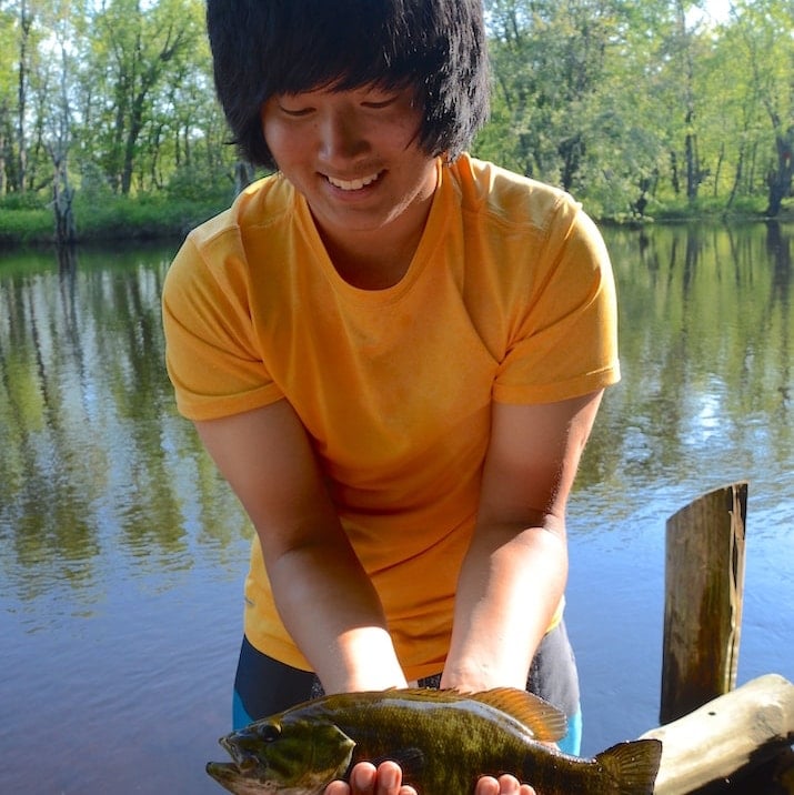 A young person holds a recently caught smallmouth bass
