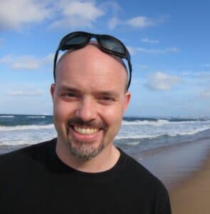 Headshot of Chez Chesak standing on a beach