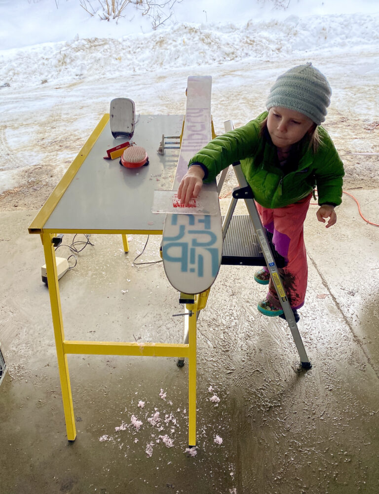 A young girl waxes a ski