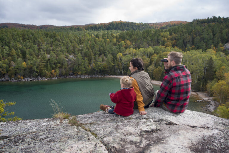 A man, woman, and child sit on a rocky lookout above a lake