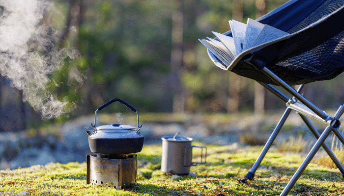 A pot steams at a campsite next to a camping chair.