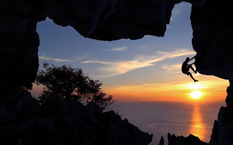 A rock climber at sunset climbing rocks near a lake