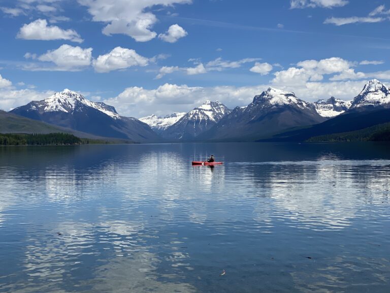 A kayaker in clear blue water with mountains in the distance