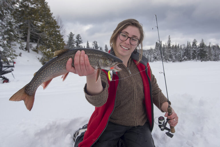 A woman in a wintery setting holds a fish towards the camera