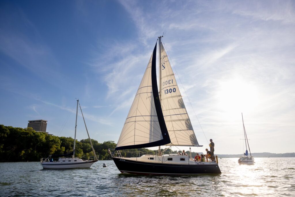 A sailboat sits in the centre of the frame, on a clear day with the sun behind it