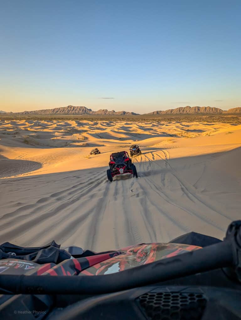Three dune buggies cross the desert, seen from the POV of the front of another dune buggy