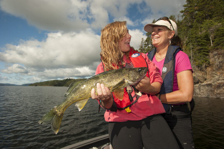 A smiling woman stands behind a child who is holding a large fish